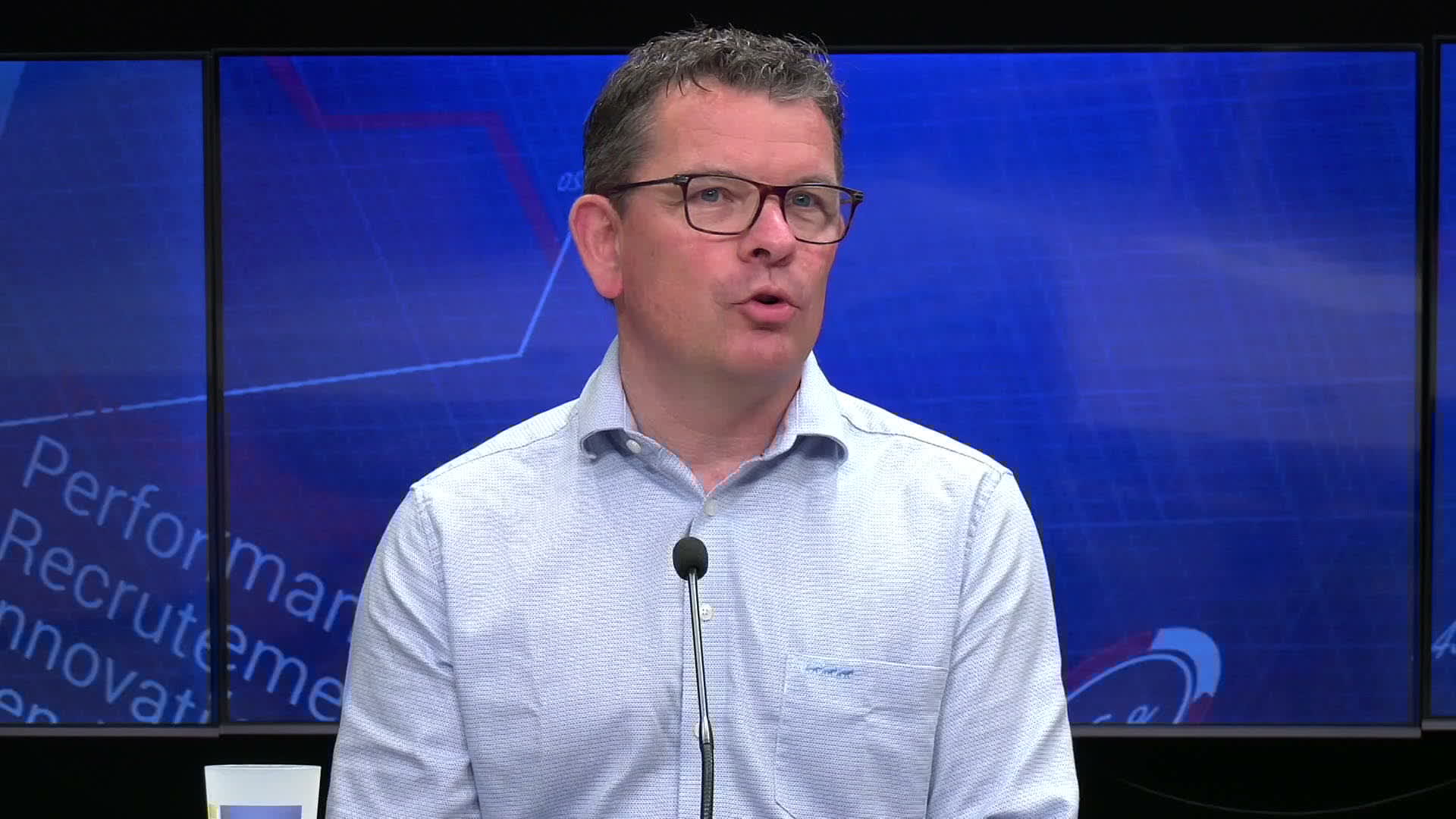 Homme en chemise claire parlant devant un micro sur le plateau de Réussites le mag