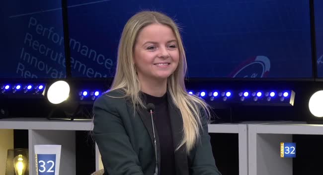 Invitée souriante sur le plateau de Réussites le mag avec micro et éclairage en fond